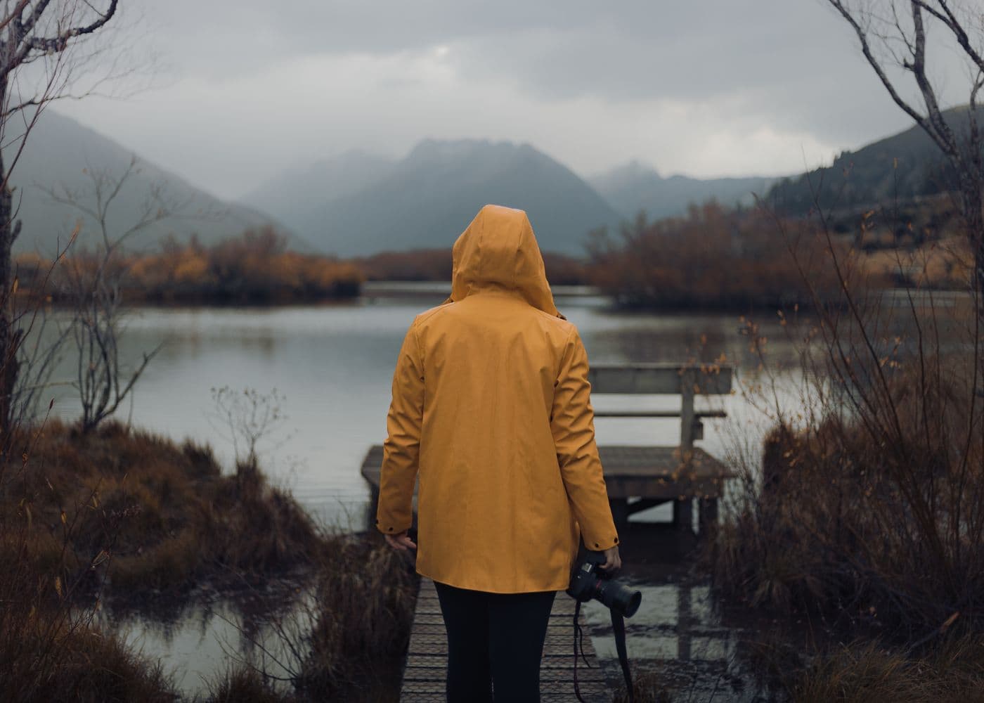 Person in a yellow raincoat beside a mountain lake in rainy weather