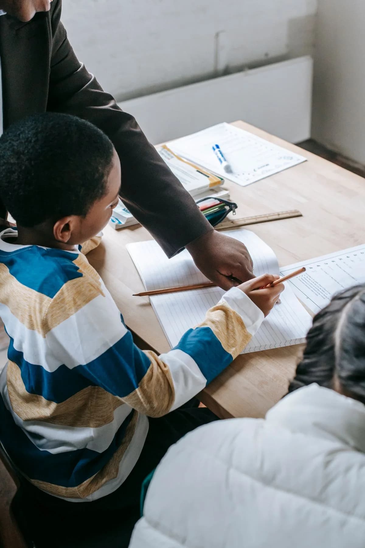 An adult helping children with written schoolwork at a desk