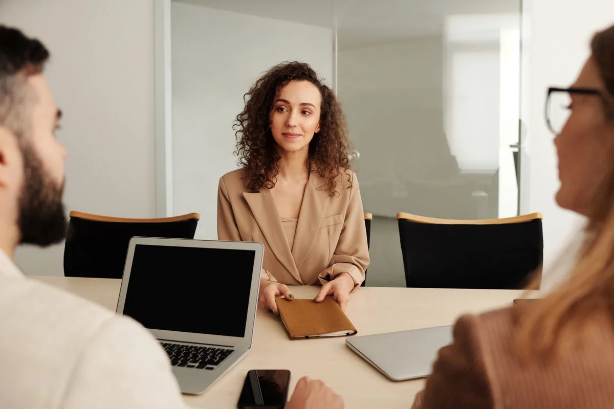 A woman speaking with interviewers across a table