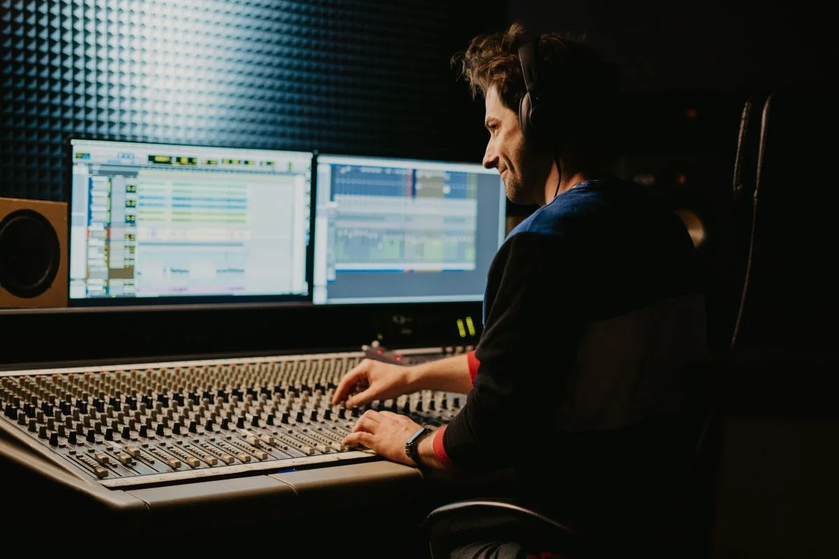 A sound engineer wearing headphones at a studio mixing console
