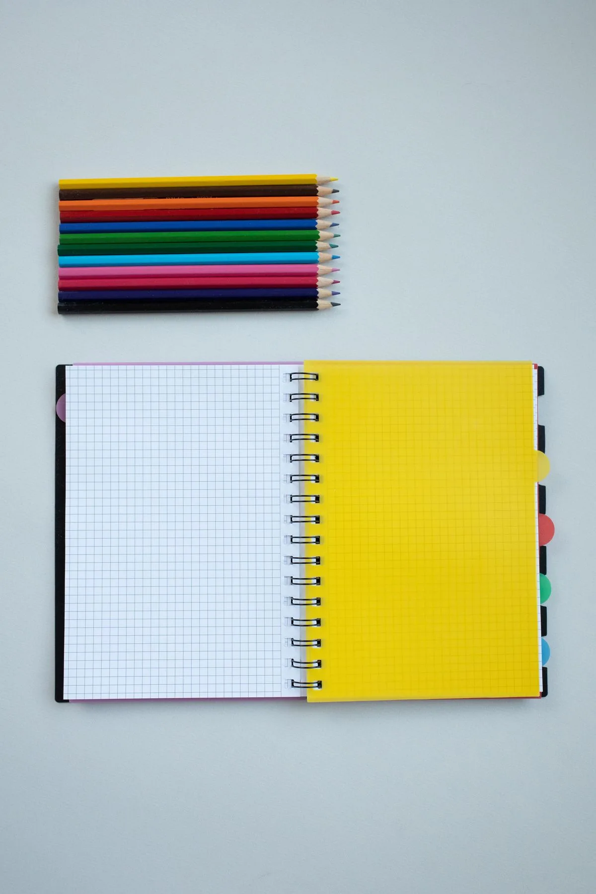 Coloured pencils beside an open spiral notebook